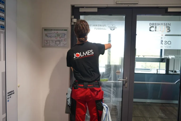 Mitarbeiterin im Jolmes Shirt reinigt eine Glastür