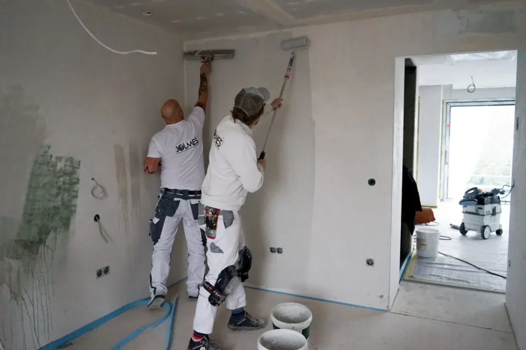 Zwei Jolmes Maler spachteln und rollen eine Wand